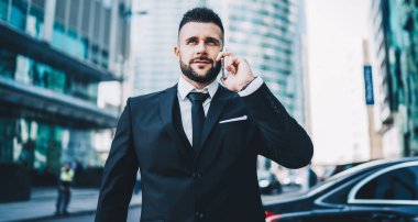 Finansal bölgede ciddi bir girişimci cep telefonuyla iletişim kuruyor. Şehir merkezinde iş ortağını bekliyor. Takım elbiseli beyaz bir erkek.