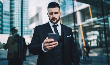 Ciddi yönetici 30 yaşında. Akıllı telefondan iş hakkında haber okuyor. Finansal bölgedeki bina yakınında 4G internet kullanan cep telefonu kullanıyor.