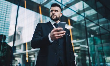 Kafkasyalı hükümet çalışanı elinde cep telefonu cihazıyla içerik web sitesinden finansal haberleri inceliyor ve cep telefonuyla ilgili düşünceli bir uzman.