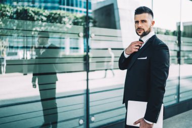 Yakışıklı erkek girişimcinin yarı boy portresi dizüstü bilgisayarla şehir merkezinde kameraya bakıyor ve kravat takıyor, kendine güvenen iş adamı dışarıda bilgisayar uzmanı olarak bekliyor.