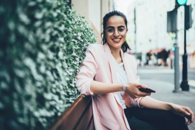 Cep telefonu aygıtındaki kablosuz bağlantıyı kullanarak sosyal ağdaki takipçilerle iletişim kurarken kameraya gülümseyen mutlu seyahat blogcusu, gezi sitesinden cevap bekleyen hippi kız