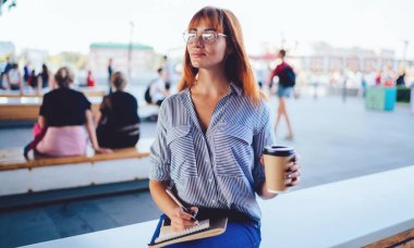 Öğrenciler için makaleler yazan düşünceli kadın yazar dışarıda oturuyor ve kahve saatinde yayın için fikirler üzerinde düşünüyor, ders kitabı ile birlikte beyaz hippi kız üzerinde kafa yoruyor.