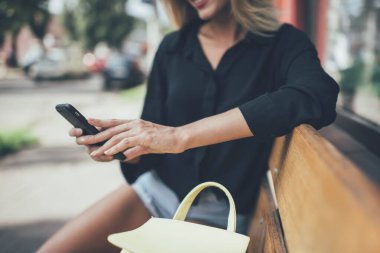 Milenyum yeniyetme kızın akıllı telefon klavyesiyle metin içeriği yazarken görüntüsü kesildi. Şehir bankında dinlenirken ve internet bağlantısı kurarken, kadın blogcu yayın yapıyor.