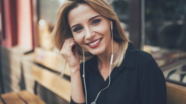 Müzik hobisi için zaman harcarken sevimli gülümseyen ve beyaz dişleriyle kameraya bakan güzel bayan meloman portresini yakından çek. Elektronik kulaklıklı mutlu sarışın kadın dışarıda poz veriyor.