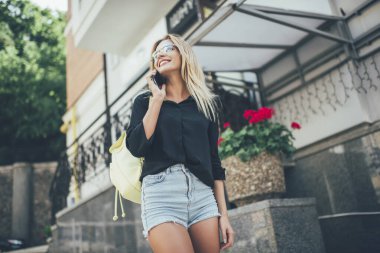Heyecanlı kadın gezginlerin günlük kıyafetleriyle en iyi arkadaşına yaz tatilleri hakkındaki izlenimlerini paylaşması için seslenmesinin altında, pozitif hipster kız uluslararası arama için gezici bağlantısını kullanıyor.