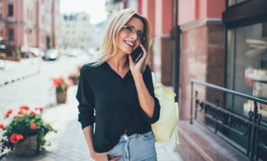 Hoş gülüşü olan neşeli bir kadın cep telefonuyla dostça sohbet ederken kendini iyi hissediyor. Seyahatler sırasında şehir ortamında günlük kıyafetlerini giymiş mutlu bir beyaz kadın.