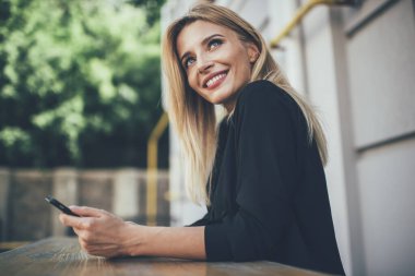 Teknoloji ve nesil kavramı, açık havada dinlenirken yüzünü çeviren samimi gülümsemesi olan çekici bir kadın. Çevrimiçi iletişim için cep telefonu tutan pozitif sarışın hippi kız.