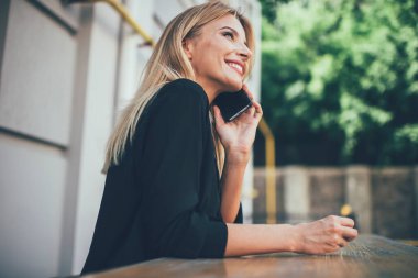 Heyecanlı gülümseyen kadın, boş zamanlarında cep telefonundan iyi haberler duymaktan mutlu, duygusal beyaz kız cep telefonuyla en iyi arkadaşına başvuru yoluyla telefon ediyor.