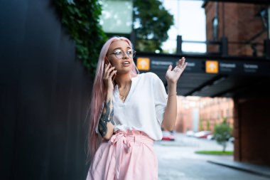 Görme düzeltmesi için optik gözlüklü çekici bir kadın akıllı telefon cihazıyla telefon ederken en iyi arkadaşıyla şok edici bilgiyi tartışıyor. Gezgin, genç ve güzel bir hippi kız.