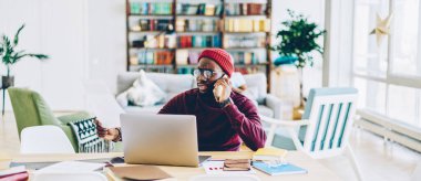 Kızgın Afrikalı Amerikalı erkek elinde kağıt tutmaktan ve telefonla konuşmaktan memnun değil. Koyu tenli, serbest çalışan, servis operatörüyle evdeki faturalar hakkında cep telefonu görüşmesi yapıyor.