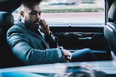 Ciddi Afrikalı Amerikalı bir adam iş ortağıyla buluşma yeri ve takılabilir kol saati için iletişim kuruyor. Resmi kıyafetli bir adam araba gezisi sırasında cep telefonu kullanıyor.