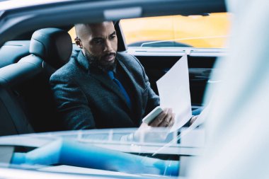 Koyu tenli erkek strateji uzmanı şirket geliştirme planı oluşturmak için bilgileri kontrol ediyor. Ofis binasına giden yolda çalışıyor. Otomobil okuma sözleşmesindeki iş yolcusu.