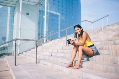 Sıradan giyinmiş heyecanlı hippi turist şehir setinde fotoğraf ekipmanlarıyla oturuyor ve boş zamanlarında kameraya gülümsüyor. Yüzünde güzel bir gülümseme olan neşeli İspanyol kadın.