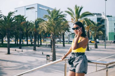 Şık güneş gözlüklü çekici kadın turistin yarı boy portresi şehir ortamında duruyor ve online arama için gezici uluslararası bağlantıyı kullanıyor, uygulamayla iletişim kuran genç kadın