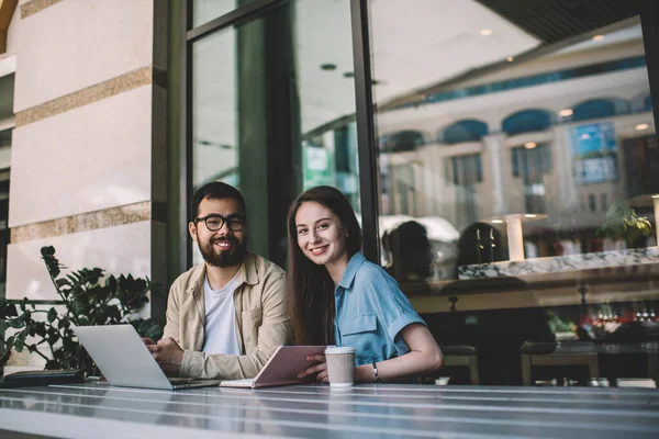 Üniversite kursunda işbirliği yapmak için yetenekli hippi çocuklardan oluşan sokak kafeteryasında toplanan mutlu milenyum arkadaşları dizüstü bilgisayarları ve eğitim kitaplarıyla masaya oturuyor ve kameralara gülümsüyor.