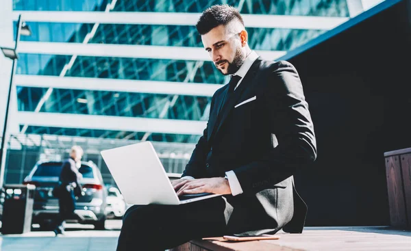 Şirketin başarılı erkek patronunun şirket sitesindeki finansal belgeleri araştırmak için dizüstü bilgisayarını kullanırken kamu interneti kullanarak internet üzerinden çalışan akıllı tüccarın web sitesindeki bilgileri güncellemesinin yan görüntüsü