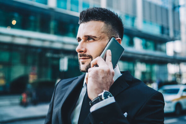 Вид сбоку кавказский бизнесмен, общающийся с оператором во время поездки стоя в центре мегаполиса и используя 4g беспроводной в роуминге, концепция международного разговора по мобильному телефону
