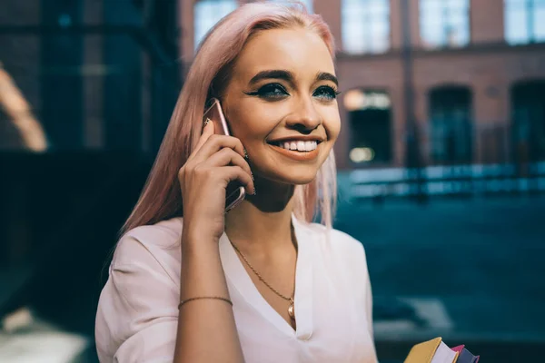 フレンドリーなスマートフォンの会話の間に笑ってピンクの髪を持つ陽気なヒップスターの女の子 顔にかわいい笑顔で肯定的な女性ティーン離れて見て 携帯電話を介して話して 100万人の人々 — ストック写真