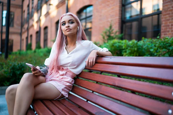 Düşünceli bin yıllık hippi kız ilginç bir ses kitabı üzerinde kafa patlatırken düşünceli bir şekilde başka tarafa bakıyor. Pembe saçlı genç bir kadın, kulaklıkla dinleme kaydıyla bankta dinleniyor.