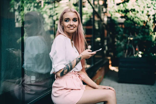 Başarılı yeniyetme kız bakışlarını kaçırıyor ve sosyal ağda yayınlanmak için heyecanlı bir fikir düşünüyor, moda dövmeli, iletişim için cep telefonu aleti tutan olumlu milenyum kadını.