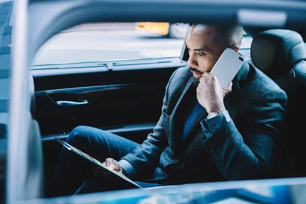 Concept of international roaming internet connection for business communication with partners, African American man phoning to operator for consultancy about app on digital gadget during car drive
