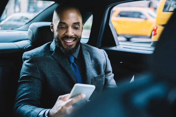 Başarılı sakallı adam elinde dijital bir alet tutuyor ve ofis arkadaşlarıyla mesajlaşırken gülümsüyor. Cep telefonuyla interneti taramak için 4G kablosuz ağ kullanıyor. Otomobildeki iş adamı.