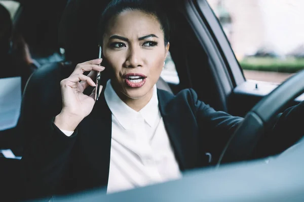 Serious female proud ceo calling to business partner for solving problems during car driving to conference with employees, puzzled woman confused with received information during cell conversation