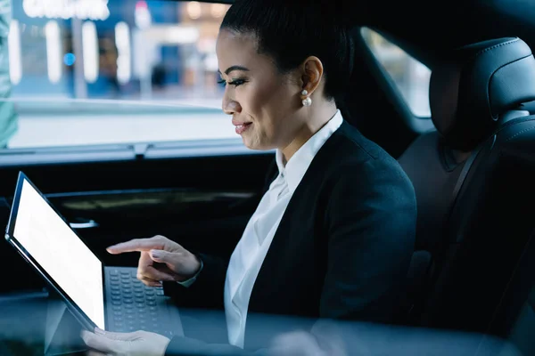 Positive female director sitting at automobile backseat and using digital tablet with portable keyboard for online communication with clients,successful woman searching files on touch pad with mock up