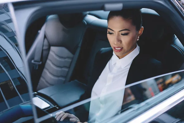 Young experienced woman financial director of company reading received email message connected to 4g on modern touch pad, female passenger on backseat of vehicle car checking news on website