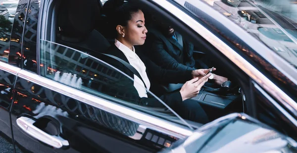 Side view of business people sitting in company car and checking smartphone messages on way to enterprise office,successful male and female entrepreneurs reading received email with detail of contract