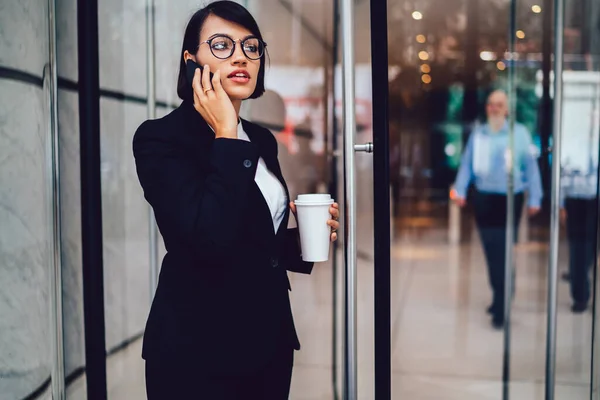 ビジネスセンター近くのスマートフォンで語るエレガントな服装で集中財務マネージャー コーヒータイム中のスタートアッププロジェクトについて電話で会話をする眼鏡の深刻な女性トレーダー — ストック写真