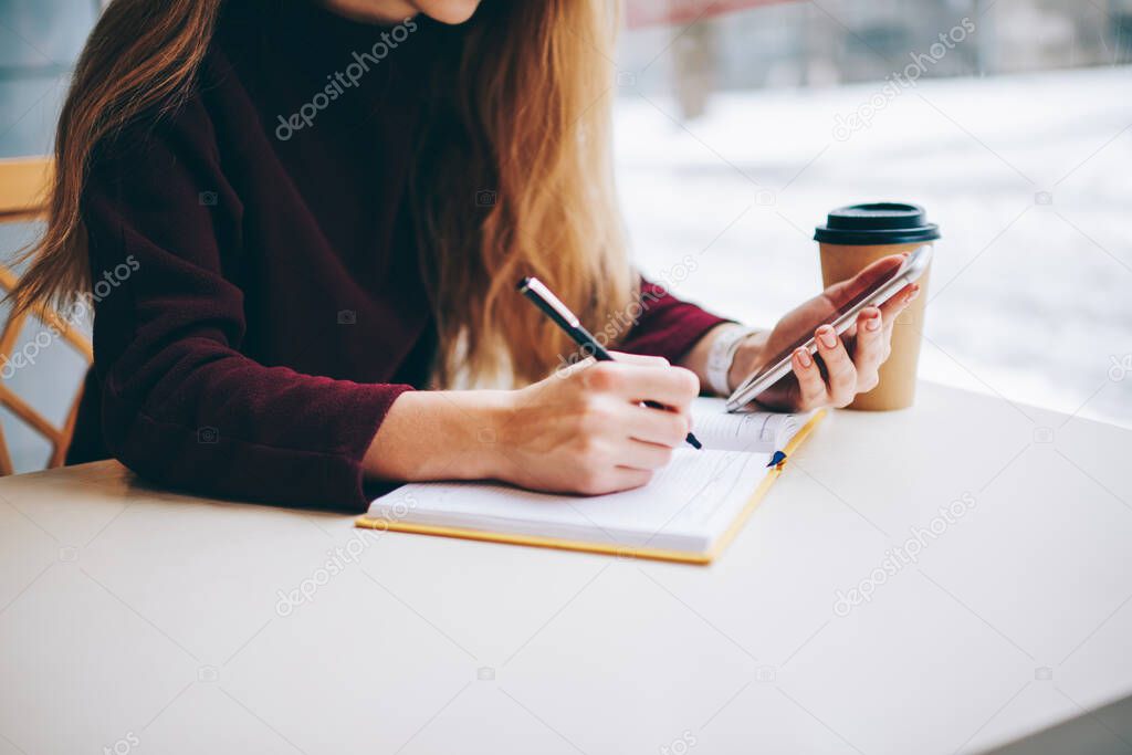 Selective focus on female student making research of information for school test via application an cellphone, hipster girl planning schedule for month while sitting in coffee shop and using phone