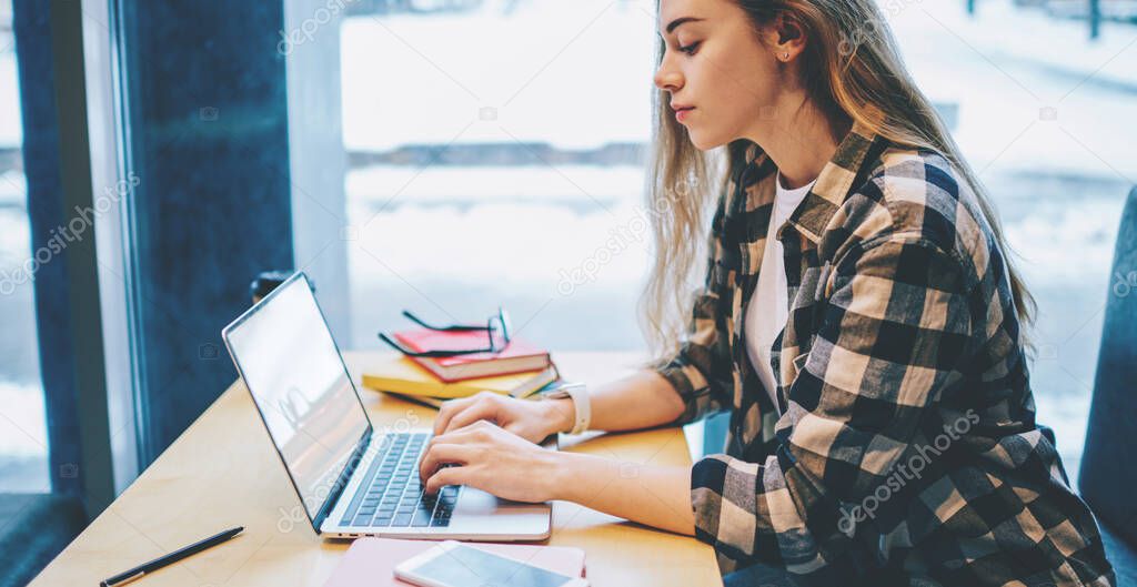 Side view of concentrated female student working on university presentation via application for creating database on laptop computer, skilled hipster girl typing text while writing mail to tutor