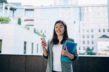Bilgiyi araştırmak için modern dijital teknolojiyi kullanan bilgili Türk kadın girişimcinin yarım boy portresi, kameraya gülümseyen cep telefonlu pozitif kadın