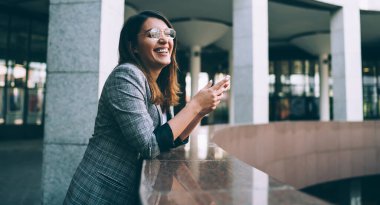 Modern cep telefonlu neşeli yeniyetme kız portresi şehir ortamında boş zamanlarında gülüyor, mutlu Türk milenyum kadını cep telefonundan içerik mesajı alıyor.