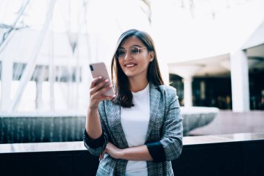 Genç gülümseyen hippi kız modern teknolojiyi şehir ortamında kullandığı için eğleniyor, mutlu kadın akıllı telefon cihazında online oyun bildirimi için kontrol ediyor.