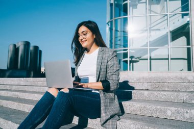 İnternet sitesindeki bir sonraki yazı için dizüstü bilgisayar uygulaması ve şehir ortamında açık kablosuz ağ kullanan çekici kadın metin yazarı, netbook 'ta online sohbetten hoşlanan pozitif hipster kız