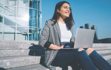 Gözlük takan neşeli Türk serbest yazar gözlerini kaçırıyor ve dizüstü bilgisayar programlarına ara verdiğinde gülüyor. Modern netbook 'lu pozitif hipster kız.