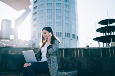 Ciddi kadın girişimciler günlük kıyafetlerini giyip online dokümanları kontrol ediyor ve detaylar için çalışanlarla uluslararası iletişim kuruyor, genç kadın cihazlarda 4G kablosuz ağ kullanıyor
