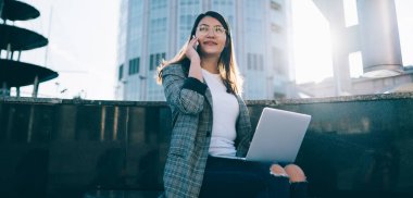 Başarılı kadın girişimci, yeni başlatılan projeyle ilgili iletişim kurmak için meslektaşına telefon ederken dizüstü bilgisayarla uzaktan çalışıyor. Cep telefonunda gezinen bağlantıyı kullanan genç bir kadın.