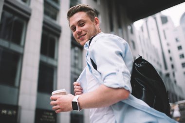 Sokakta yürürken elinde bir poşet kahve taşıyan ve kameraya gülümseyen genç pozitiften. 