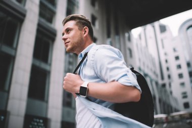 Siyah sırt çantalı yakışıklı sıradan bir adamın modern şehrin bulanık arka planında dalgın dalgın bakışıyla 