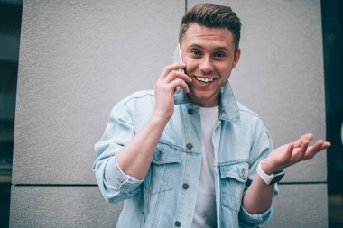 Kot ceketli havalı genç adam kameraya anlamlı bir şekilde bakıyor ve cep telefonuyla sokakta konuşurken gülüyor.