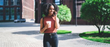 Elinde yemek fincanı olan neşeli kız öğrencinin yarım boy portresi kameraya gülümserken aynı zamanda cep telefonunda gezinen internet bağlantısını kullanarak uluslararası olumlu bir konuşma yapıyor.