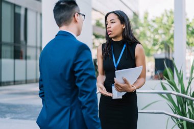 Kağıtları tutan ve iş konferansı düzenlerken erkeklerle konuşan zarif Afrikalı Amerikalı kadın sokakta duruyor. 