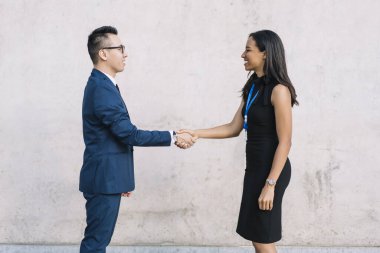 Sokağın ortasında duran ve iş konferansında el sıkışan zarif kadın ve erkeğin yan görünüşü 