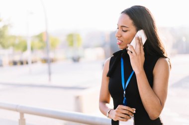 Ensesinde konferans etiketi olan zarif bir esmer ve parlak bir ışıkla sokakta dikilen bir telefon.
