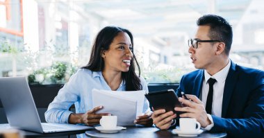 Modern kafede masa başında oturmuş iş projelerini tartışan çok ırklı kadın ve erkek aletler.