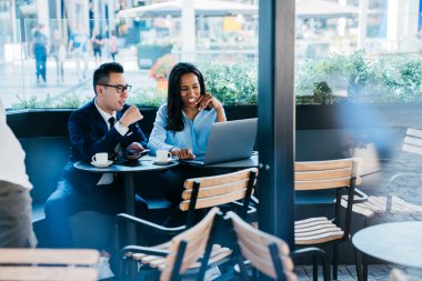 Genç, çok kültürlü bir kadın ve erkek kafeteryada oturmuş laptopla çalışıyor ve yeni iş projelerini tartışıyorlar. 