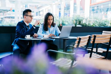 Modern etnik kadın ve erkek kafeteryada toplanıyor iş toplantısı yapıyorlar ve konuşurken dizüstü bilgisayar kullanıyorlar.